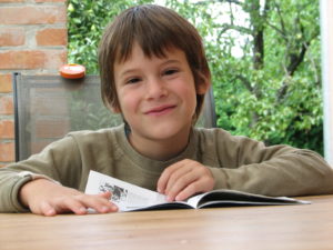 Picture of a smiling primary school-age child with book, smiling at camera
