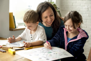 Picture of mother sitting with two children drawing and playing on ipad